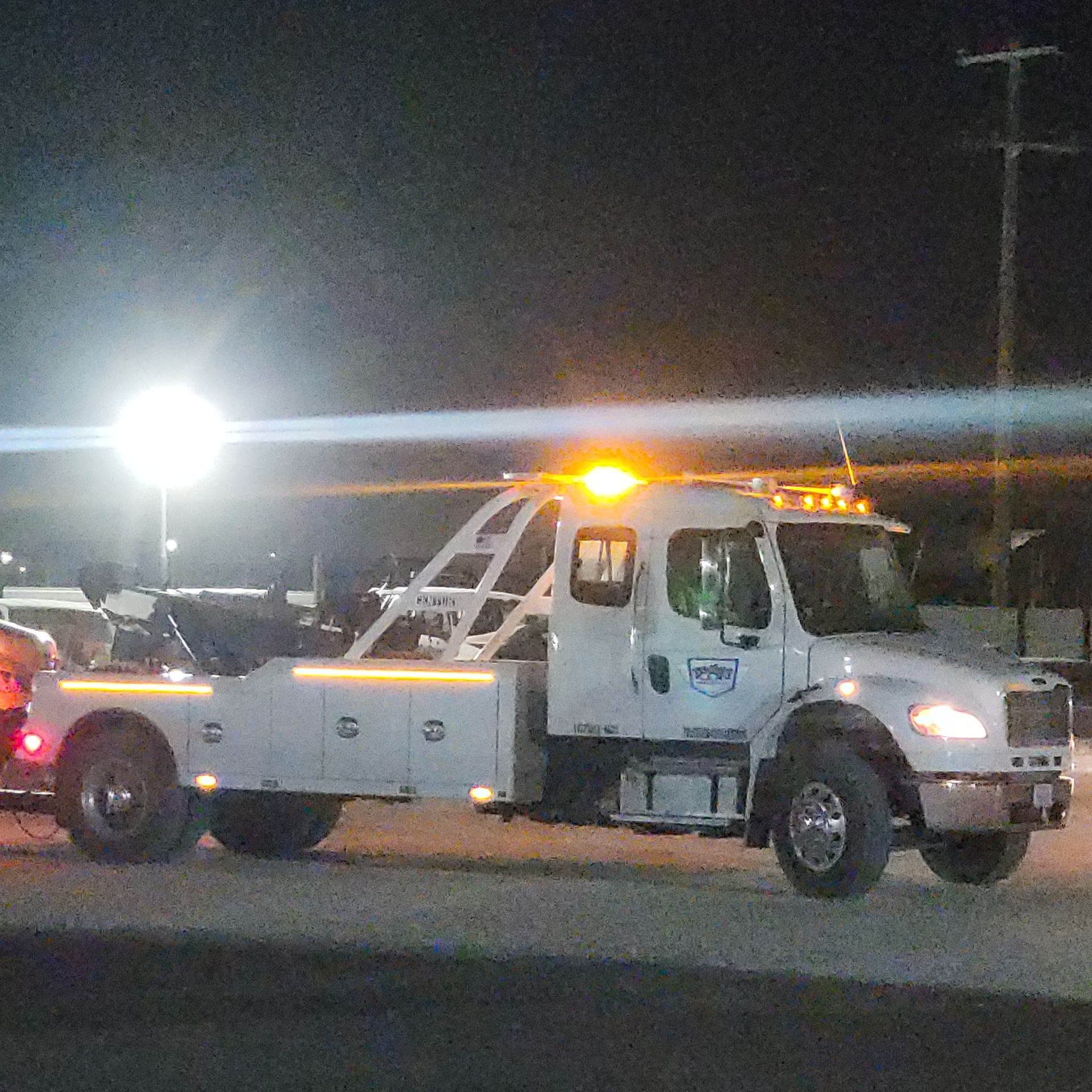 White tow truck with amber lights parked at night in a lit lot