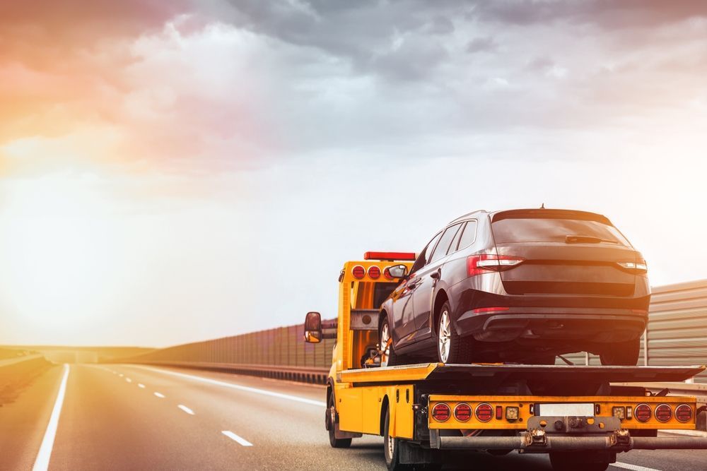 Tow truck carrying a black car on an open highway at sunset