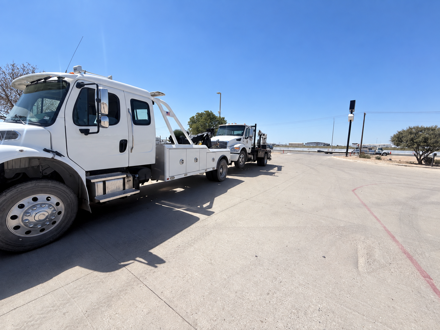 Tow truck and flatbed truck parked on a sunny roadside near a desert area