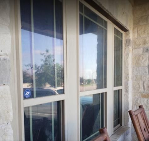 Front porch window with white trim reflecting trees and parked cars, beside stone siding and a wooden chair