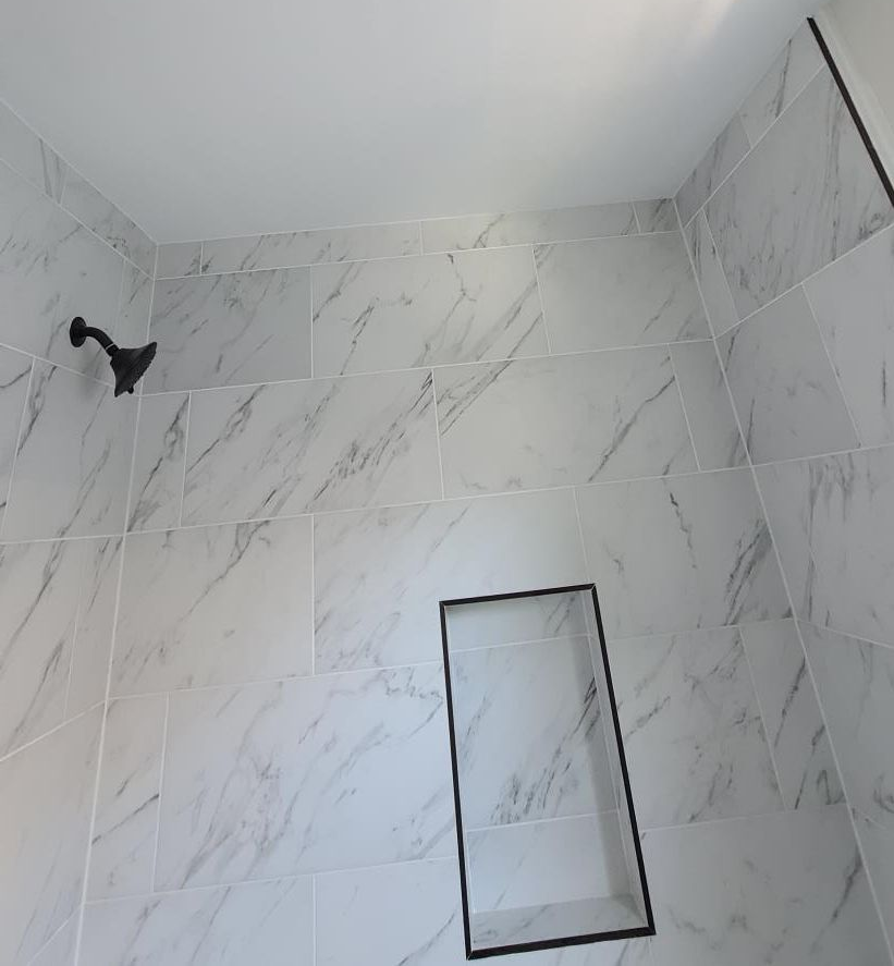 Tiled shower wall with a recessed niche and dark showerhead pipe in the corner