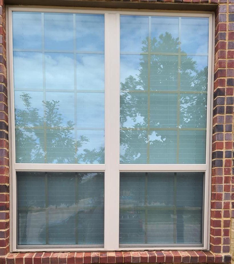 Brick house window with white trim, reflecting trees and sky