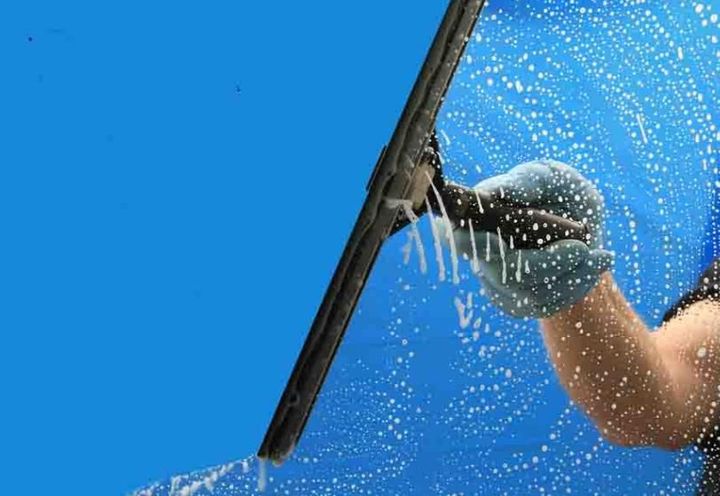 Window cleaner using a squeegee on a glass surface against a blue sky