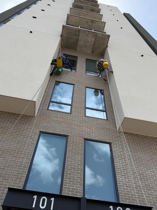 Workers on ropes cleaning windows of a tall apartment building exterior.