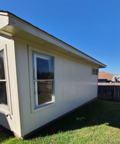 Side view of a beige house with a window, seen beside a grassy backyard and wooden fence.