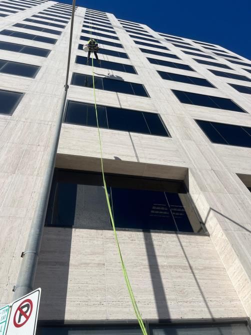 High-rise building facade with a worker suspended by a green rope near upper windows