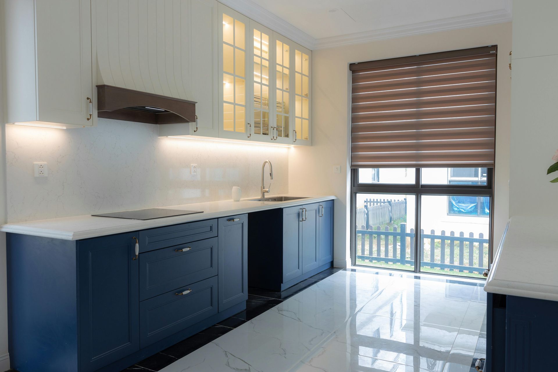 Modern kitchen with navy cabinets, white countertops, and a window with a brown blind.