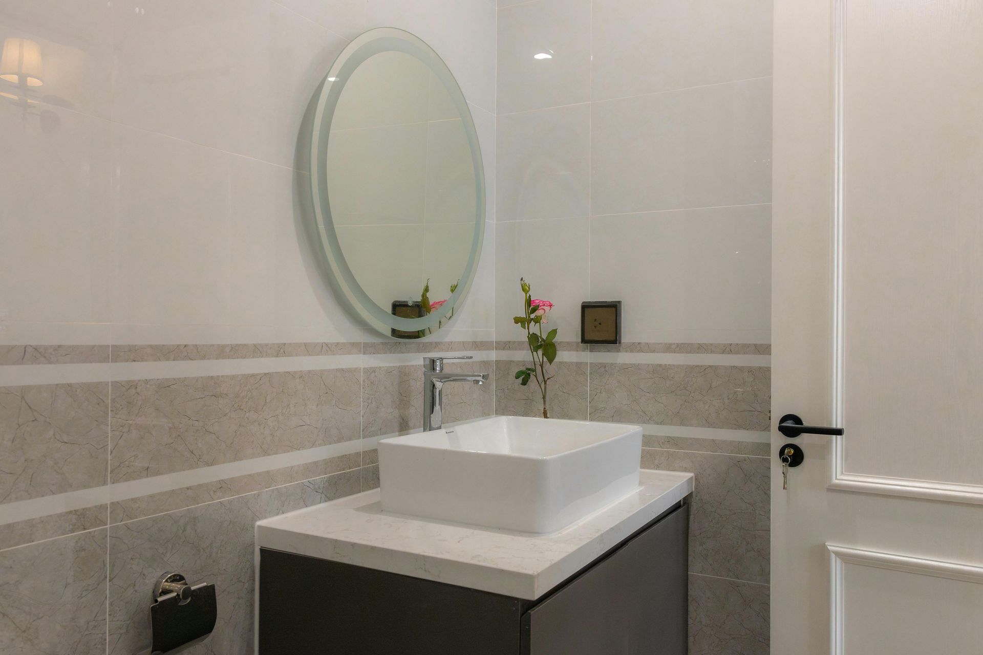 Modern bathroom vanity with oval mirror, white sink, and small flower vase