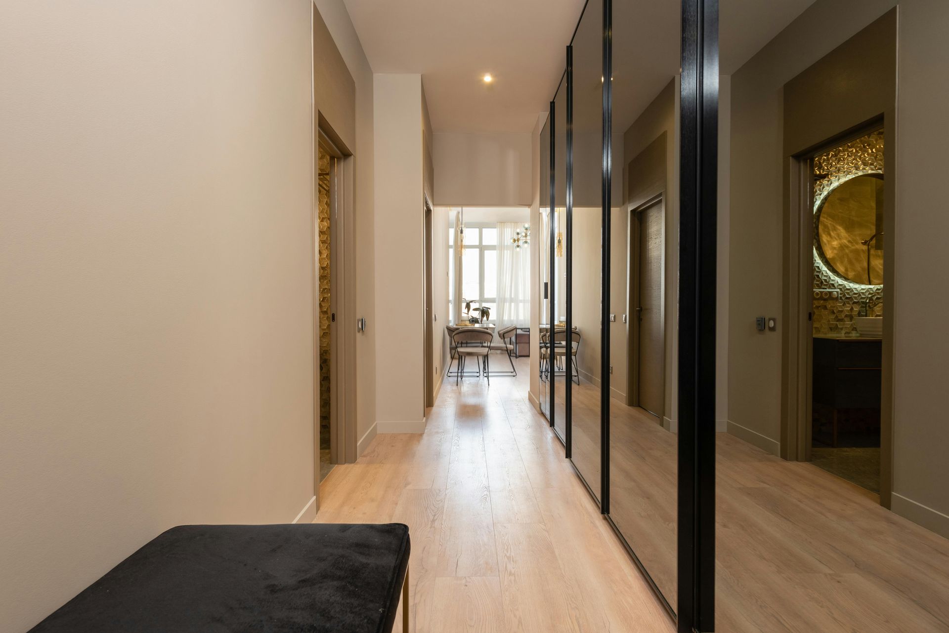 Modern hallway with wood flooring, mirrored closet doors, and a bright dining area at the end.
