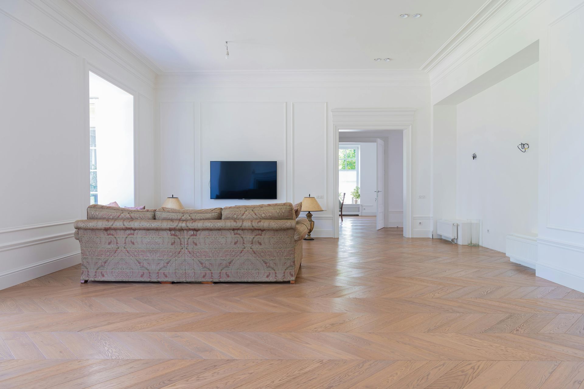 Bright empty living room with light wood floors, a beige sofa, and a wall-mounted TV