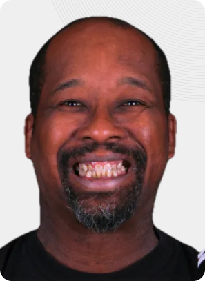 Man smiling, dark skin, short beard, visible teeth, black shirt.
