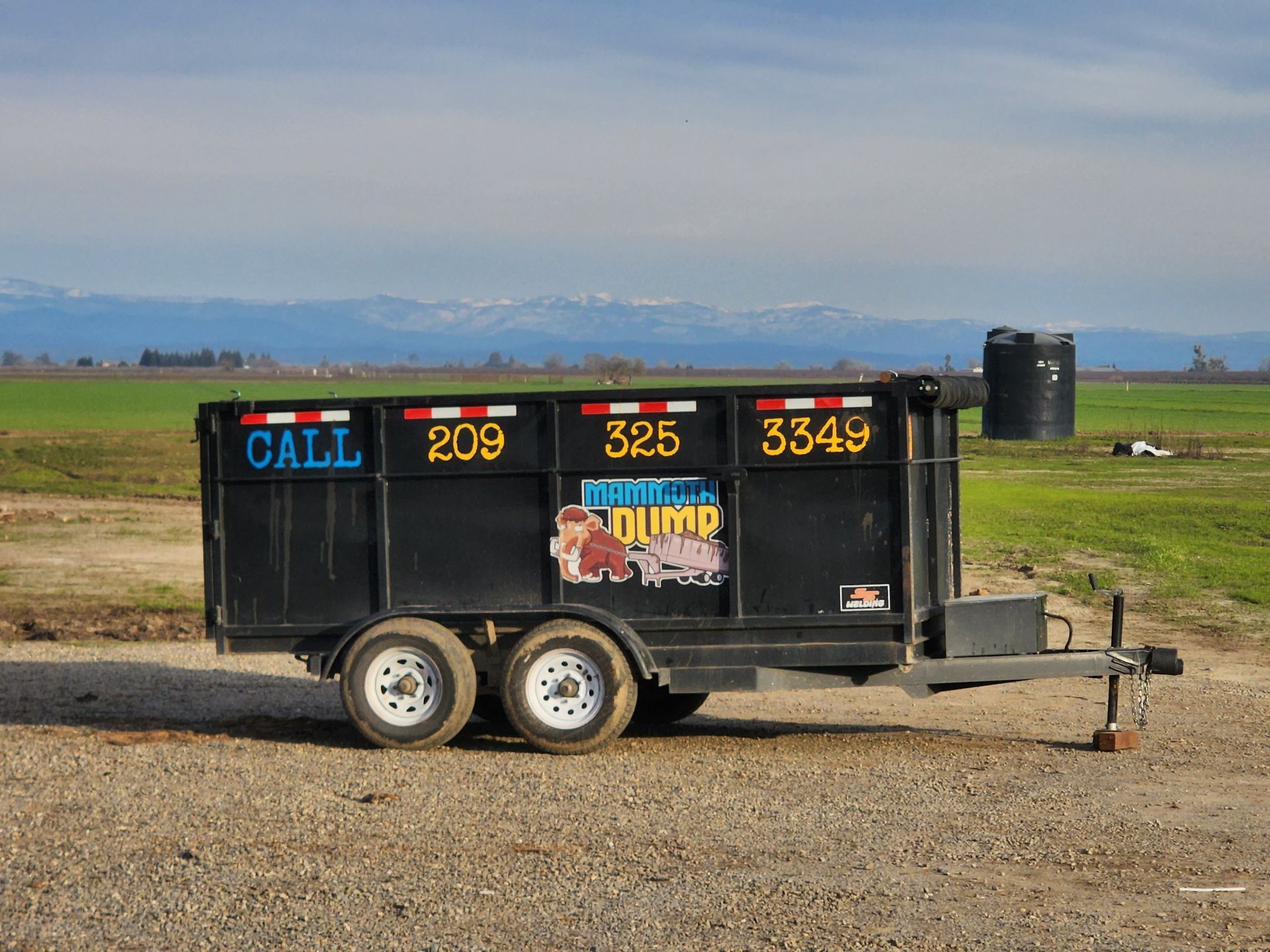 A dumpster trailer is parked in a dirt field.