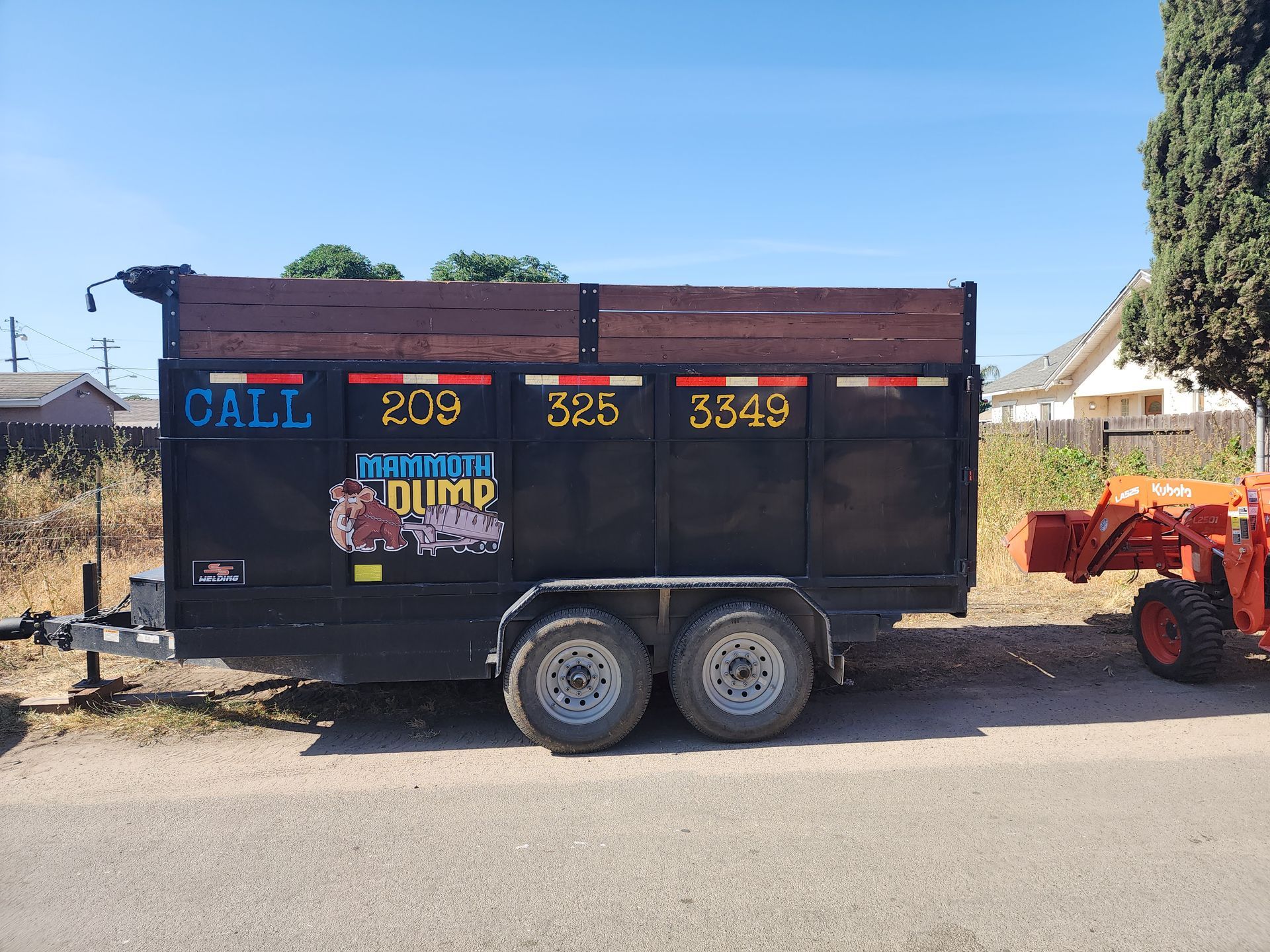 A large 20-yard dumpster stationed in front of a dead, overgrown area set to be cleared, with an ora