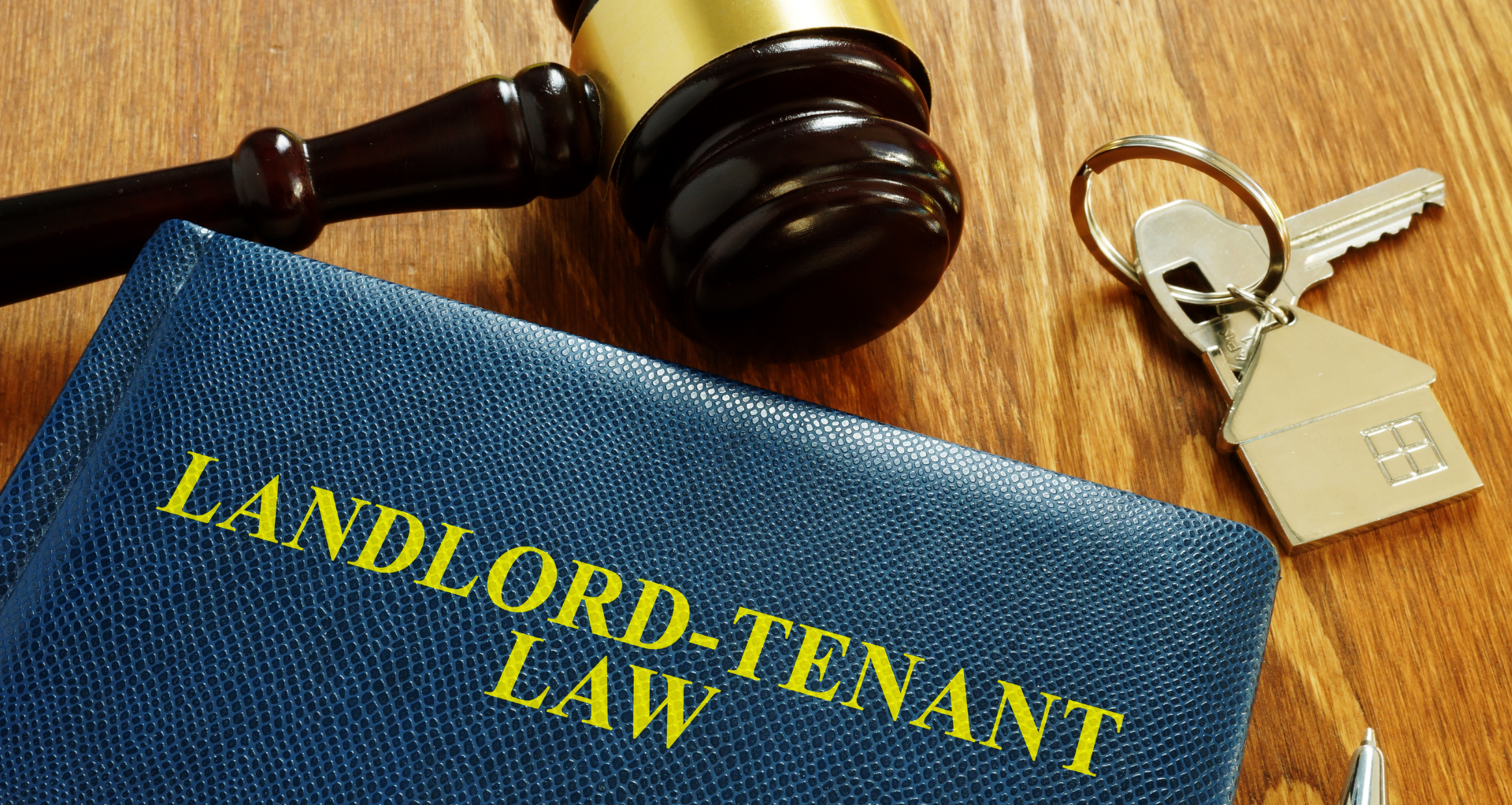 A gavel on a table alongside a set of house keys and a book titled 'landlord-tenant law'.