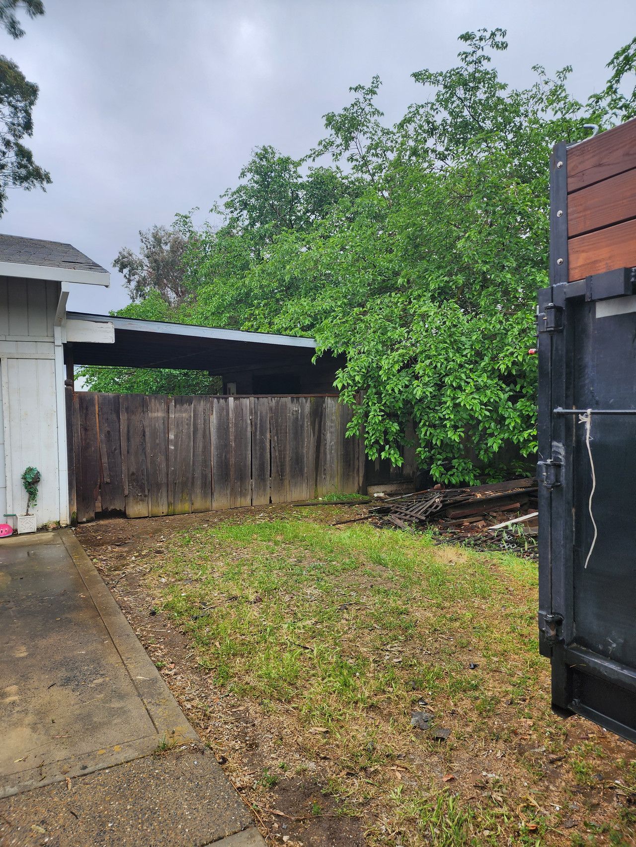 A backyard with a wooden fence and a black dumpster.