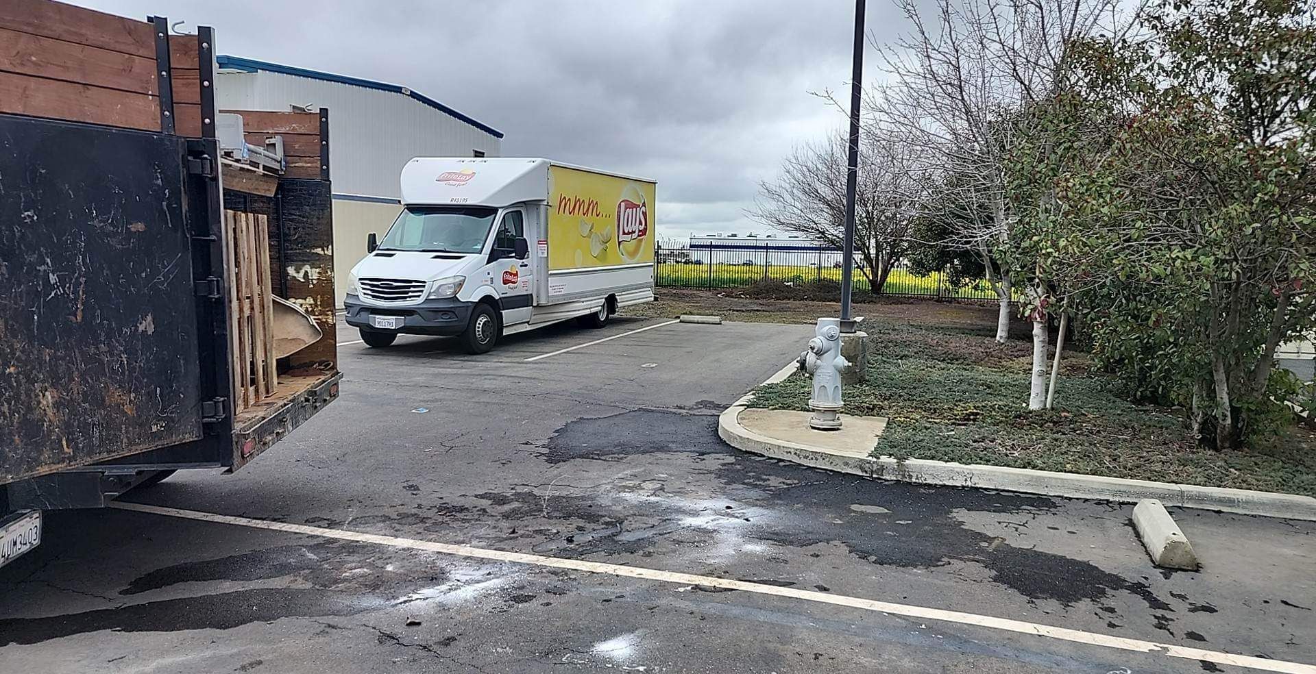 A white van is parked in a parking lot next to a dumpster.