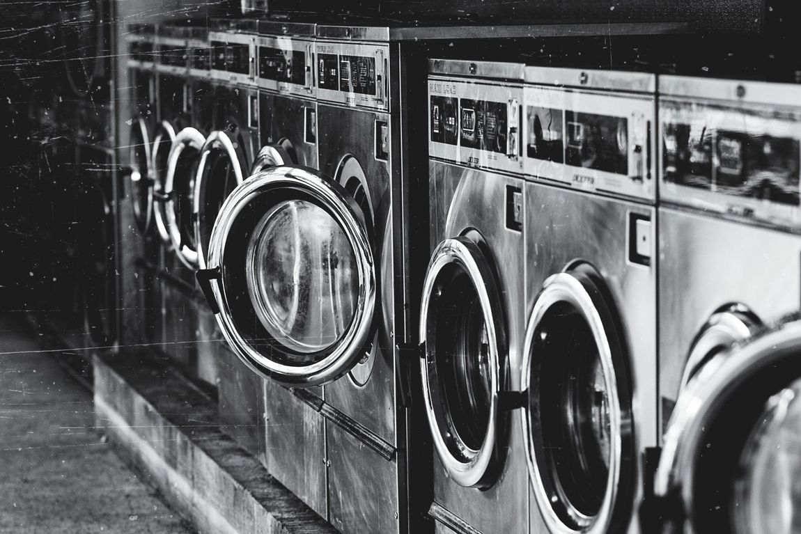 A black and white photo of a row of washing machines in a laundromat.