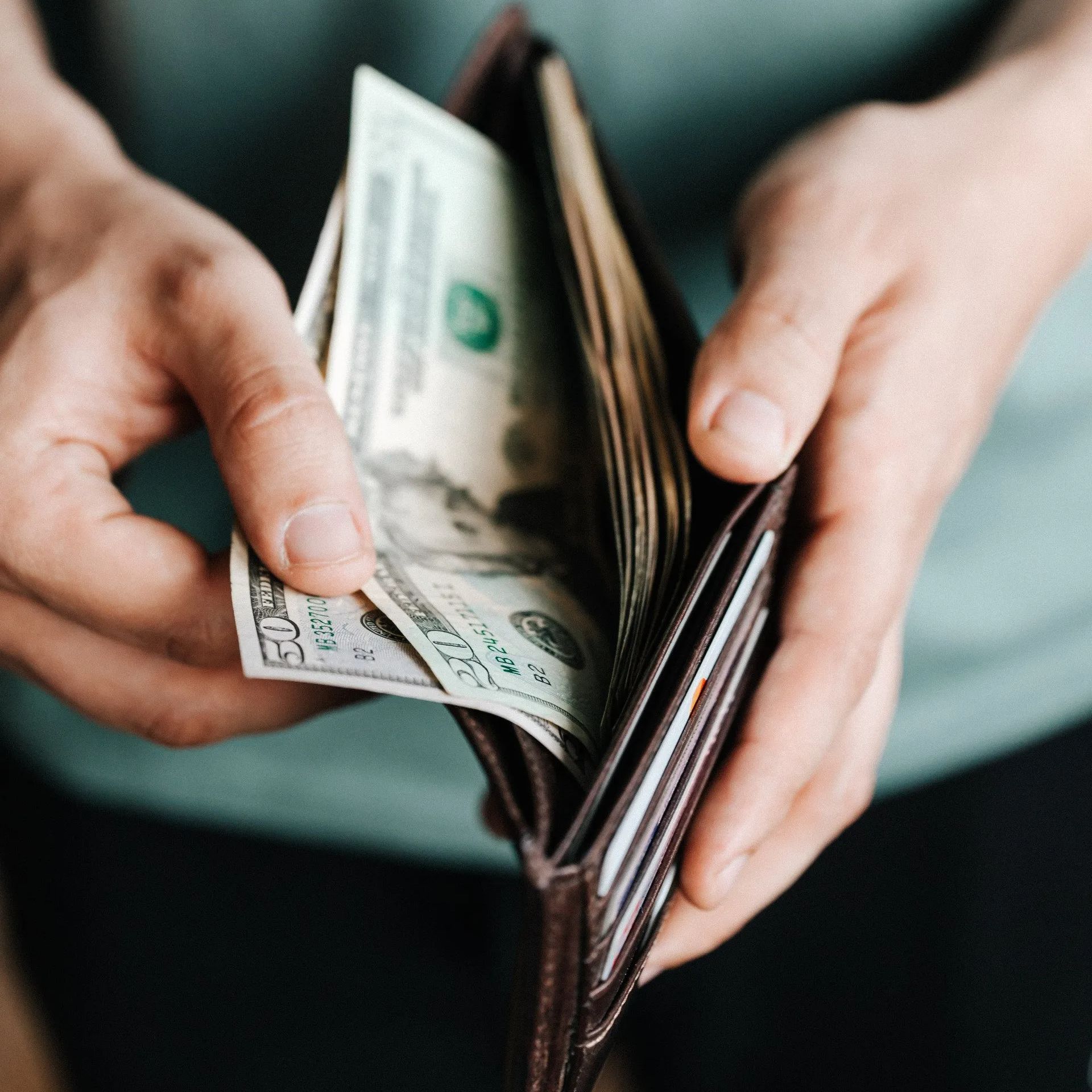 Man examining his wallet, contemplating his finances with a $50 and $20 bill visible.