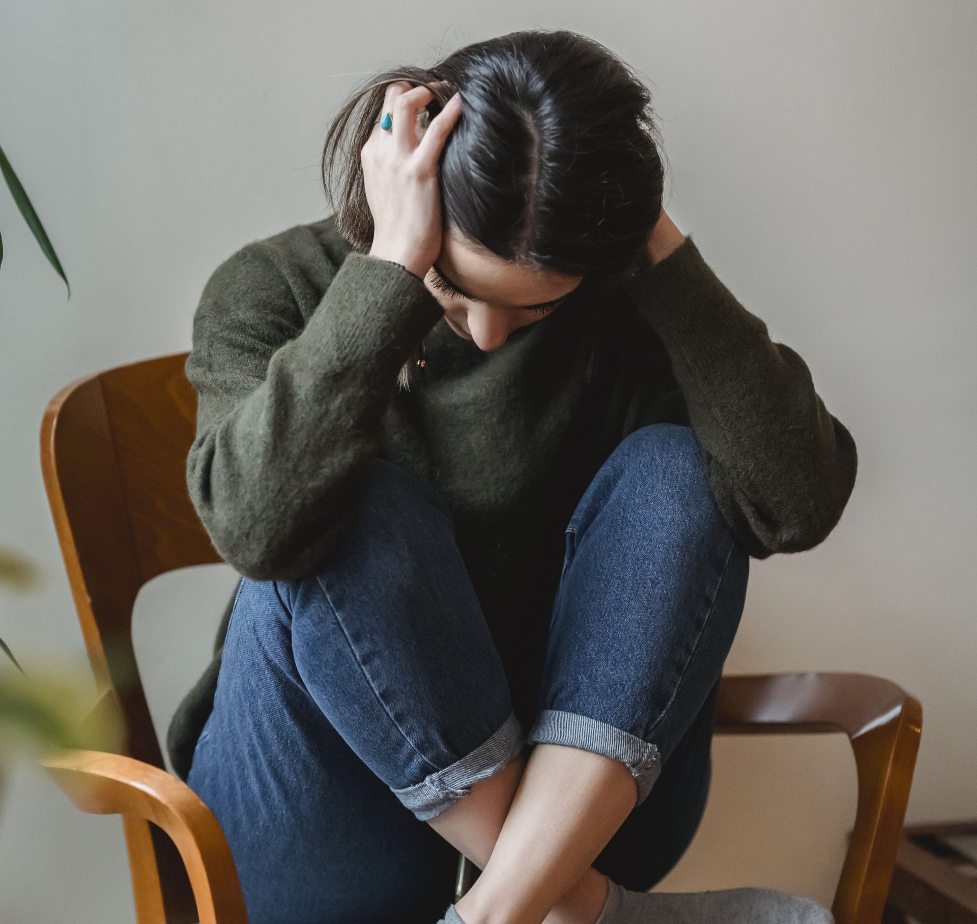 Distraught woman sitting crisscrossed on a chair with her hands on her head and her face bowed down, embodying the emotional pain of an eviction.