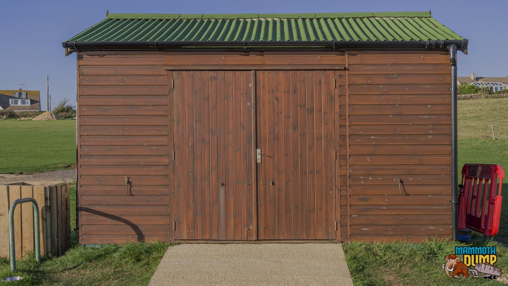 A wooden garage with a green roof is sitting in the middle of a grassy field.