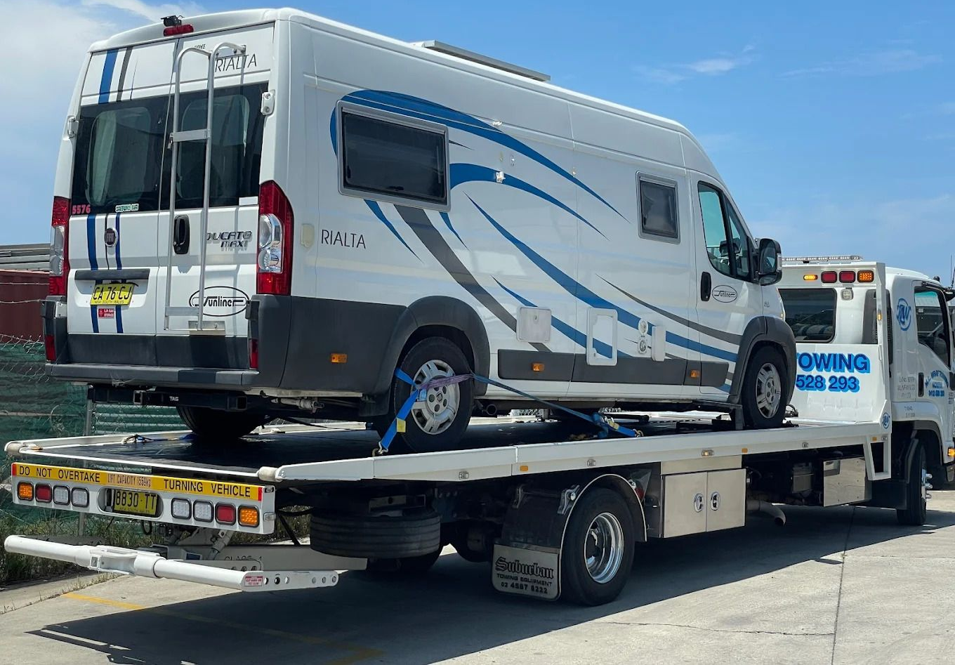Campervan on a tow truck, white with blue and grey accents, outdoors on a sunny day. — M.L. Wray Towing & Automotive Repairs in Nowra, NSW