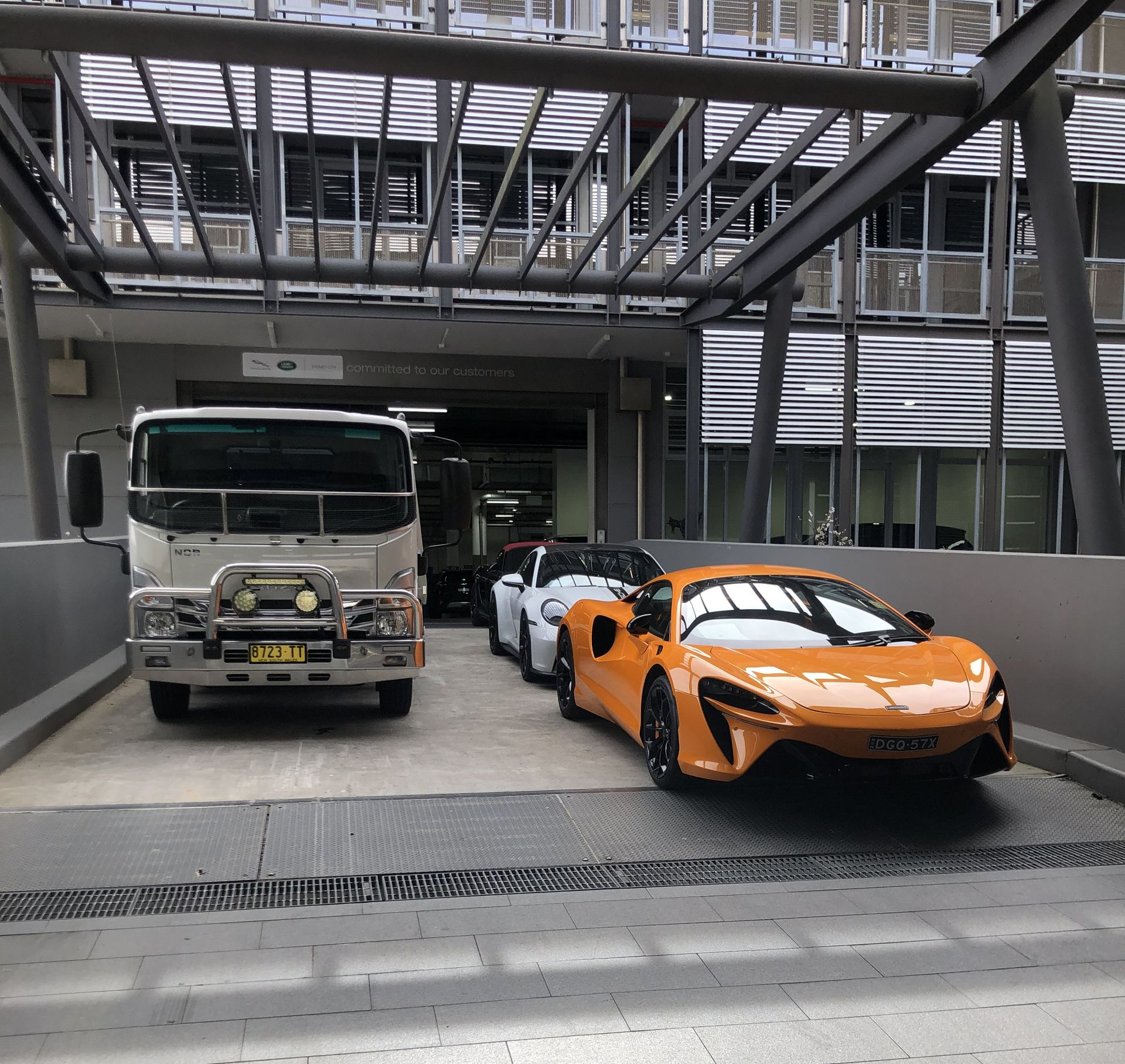 An orange sports car and two other cars parked under a building's awning next to a truck. — M.L. Wray Towing & Automotive Repairs in Kangaroo Valley, NSW