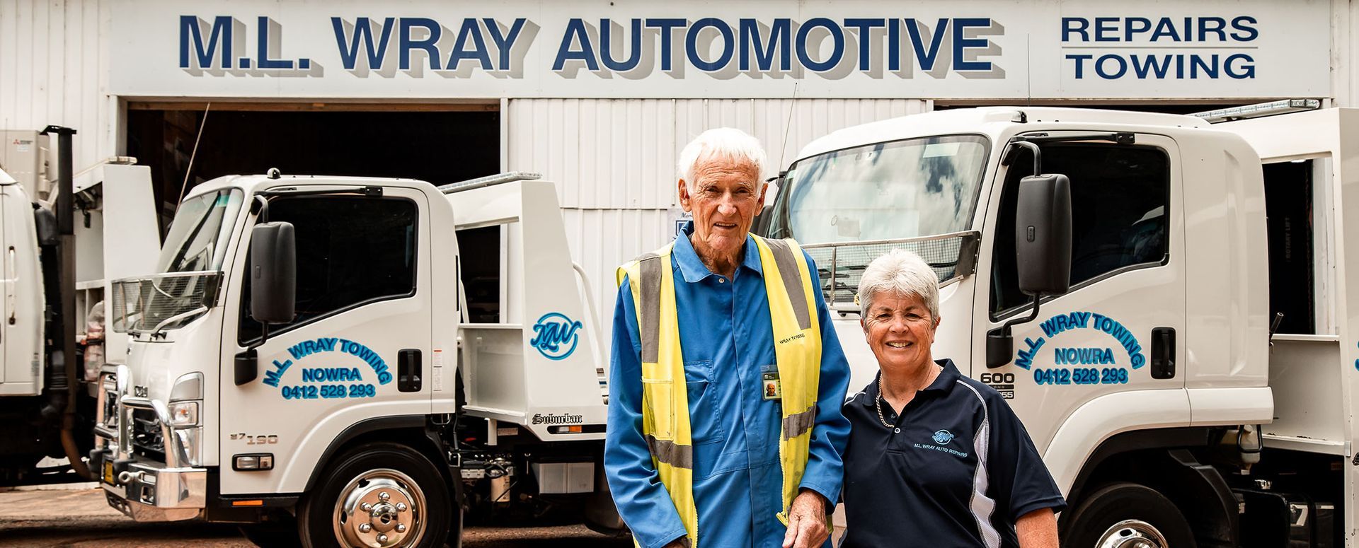 Two people stand in front of white tow trucks. The sign reads