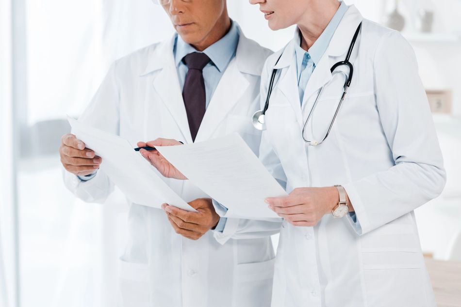 Dos médicos con batas blancas revisando documentos en un luminoso consultorio médico.