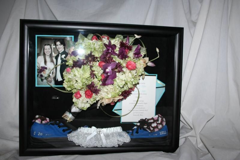 Framed memorial display with flowers, a photo, card, and folded blue cloth on a draped white background