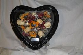 Heart-shaped black box with dried flowers and petals on white fabric background