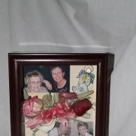 Framed collage with two portrait photos, flowers, and a colorful cartoon drawing on a gray backdrop