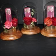 Three small glass-encased floral arrangements with pink and red roses on wooden bases against a dark background