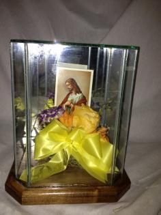 Decorative religious display in a glass case with a framed image and a yellow ribbon bow on a wooden base