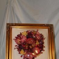 Framed floral wreath on a cream wall, with pink, red, and yellow flowers