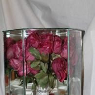 Pink flowers in a clear glass vase on a white surface, reflected in a mirrored frame.