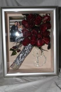 Framed bouquet of deep red roses with zebra-print ribbon and dangling pearl accents
