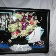 Framed display with floral garland, wedding photo, white card, and small blue-and-white shoes on a shelf