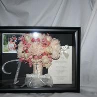 Framed wedding bouquet display with pink and white roses, invitation, and couple photo