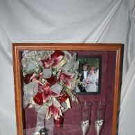Framed floral arrangement with red and white flowers, a photo, and two champagne flutes