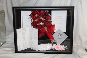 Framed memorial display with red roses, pink flowers, and folded condolence cards on a white backdrop