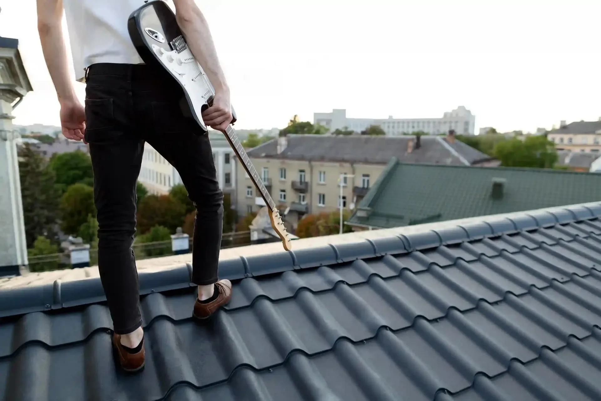 Person standing on a rooftop holding a guitar, cityscape in background.
