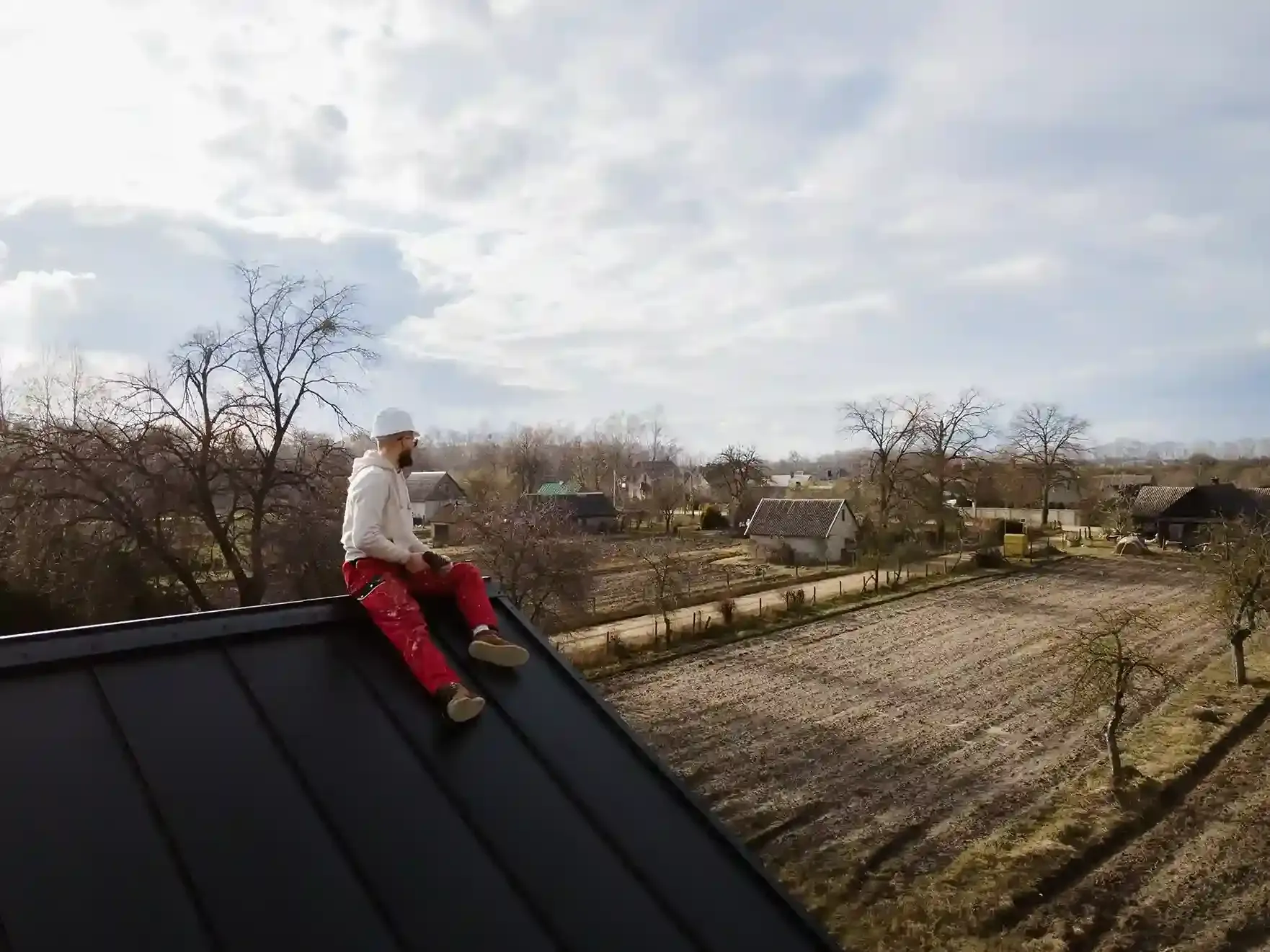 Person sitting on a dark roof, overlooking a rural landscape with fields and houses.
