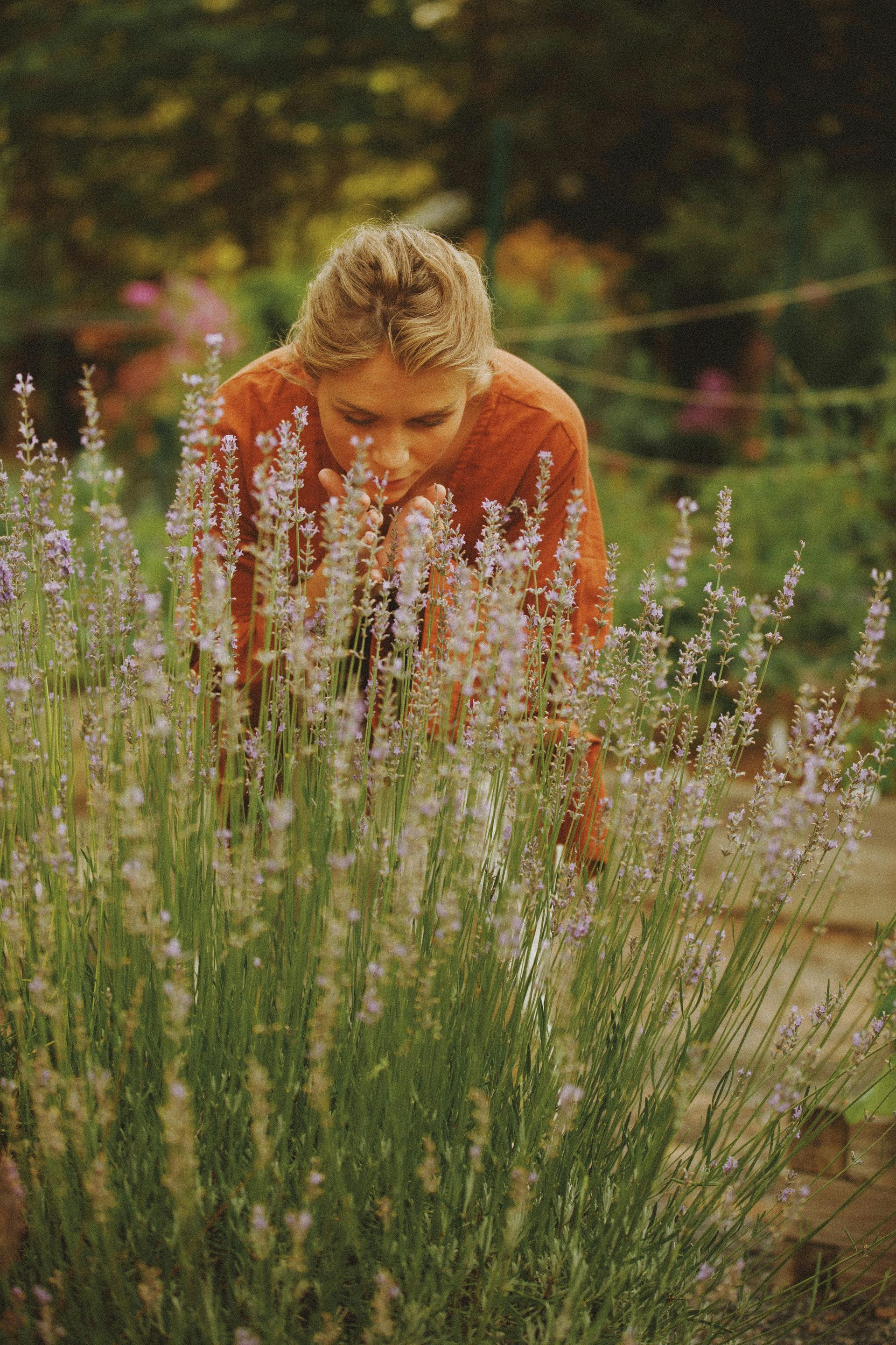 Woman leaning over and smelling lavender in a garden.