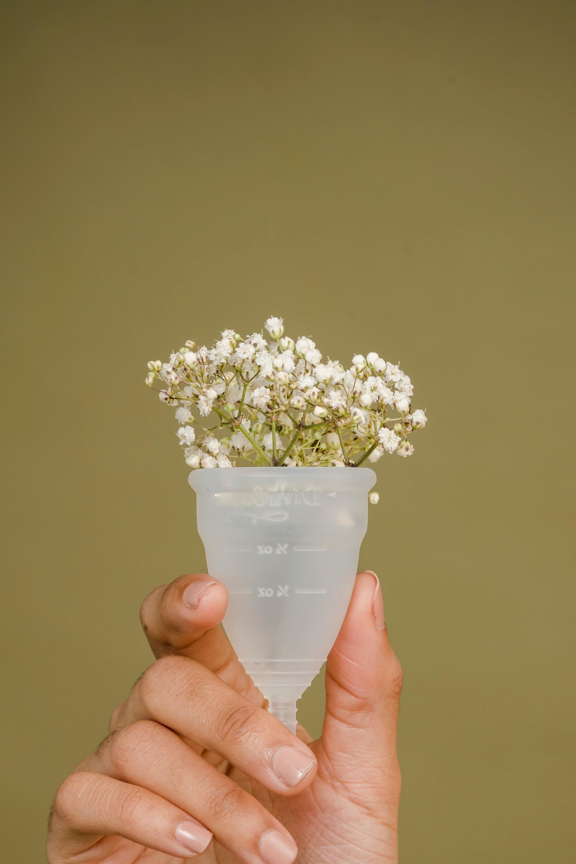 Hand holding a menstrual cup filled with white flowers against a green background.