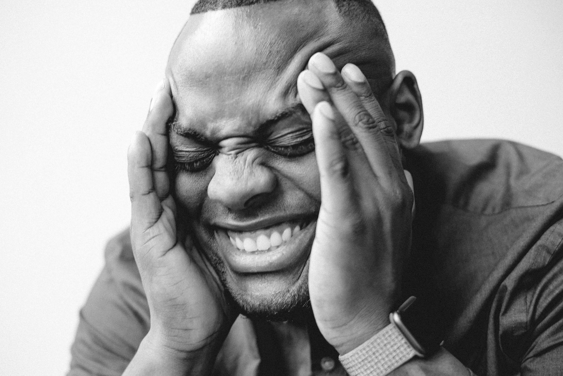 Man with hands on head, eyes squeezed shut, smiling broadly.