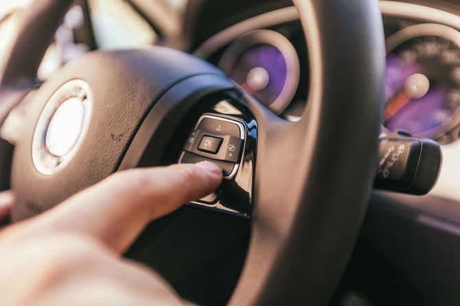 Primo piano di una mano che preme un pulsante sul volante di un'auto per azionare le funzioni del veicolo.