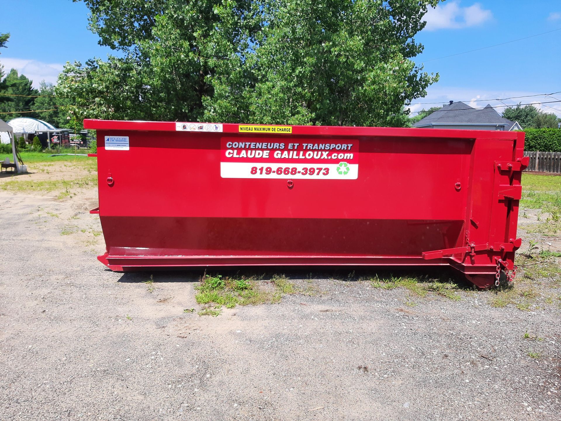 Benne à déchets rouge sur un terrain gravillonné avec des arbres en arrière-plan
