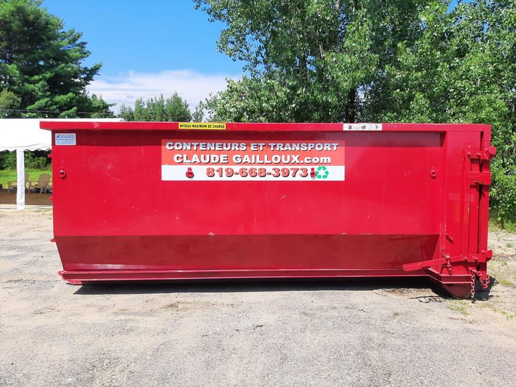 Benne à ordures rouge de chantier avec panneau d'entreprise, installée à l'extérieur par une journée ensoleillée.