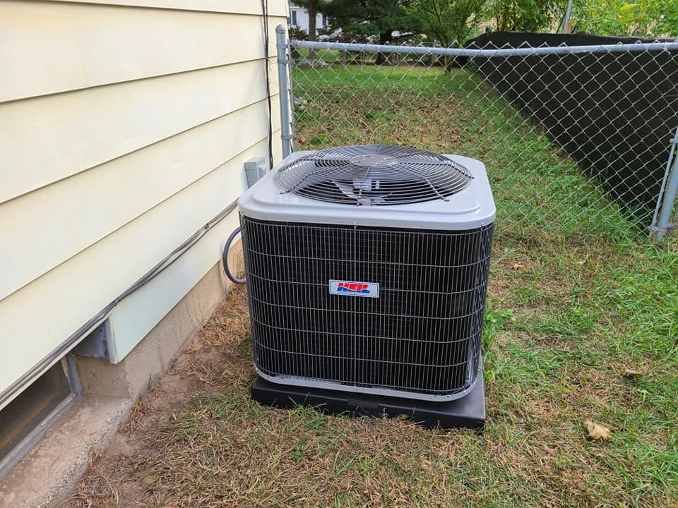 An air conditioner is sitting outside of a house next to a chain link fence.