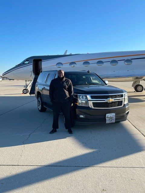 A man is standing next to a car in front of an airplane.